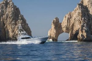Luxury yacht sailing through rocky sea arches near rugged coastline under clear blue sky